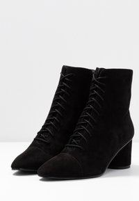 Černé semišové ankle boty s špičatou špičkou, předním šněrováním a blokovým podpatkem. Hladký povrch s matným finišem a bez viditelného loga.