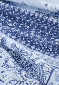 Tissu à motifs bleus présentant des designs floraux et en paisley. Des boutons sont visibles, avec des nuances variées de bleu et de blanc.