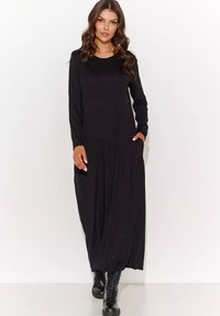 Czarna sukienka z długim rękawem, okrągłym dekoltem, zwiewną spódnicą, plisowanymi detalami i bocznymi kieszeniami, zestawiona z czarnymi botkami na sznurowadła.