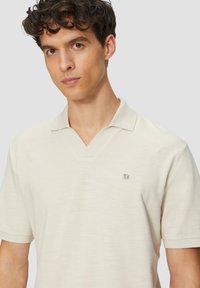 Lichtbeige poloshirt met korte mouwen en V-hals, gemaakt van een gestructureerde stof. Kenmerkt zich door een klein logoaccent op de linkerkant van de borst.