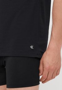 T-shirt noir en coton à manches courtes, arborant un petit logo brodé "cK" à l'ourlet, associé à un short noir ajusté.
