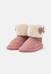 Bottines en daim rose avec un revers en crème duveteux et un petit nœud décoratif, présentant une texture douce et une semelle en caoutchouc plate.