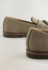 Mocassins en cuir gris au toucher lisse, à bout rond et avec un accent de nœud subtil. La semelle présente une bordure marron contrastante.