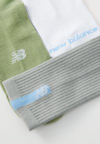 Tres pares de calcetines: verde oliva, blanco y gris claro. El calcetín gris presenta una textura acanalada, un logo y una marca en azul claro.