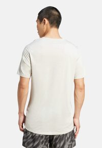 T-shirt pour homme beige clair à manches courtes, col rond et texture lisse, porté avec un short foncé à motifs.
