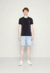 Black crew-neck t-shirt with a small pink triangle logo, paired with light blue denim shorts and white sneakers. Simple, casual outfit.