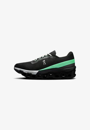 Chaussure de sport noire avec des accents verts et blancs, dotée d'un dessus texturé, d'un design en mesh et d'une semelle distinctive épaisse avec des découpes hexagonales.