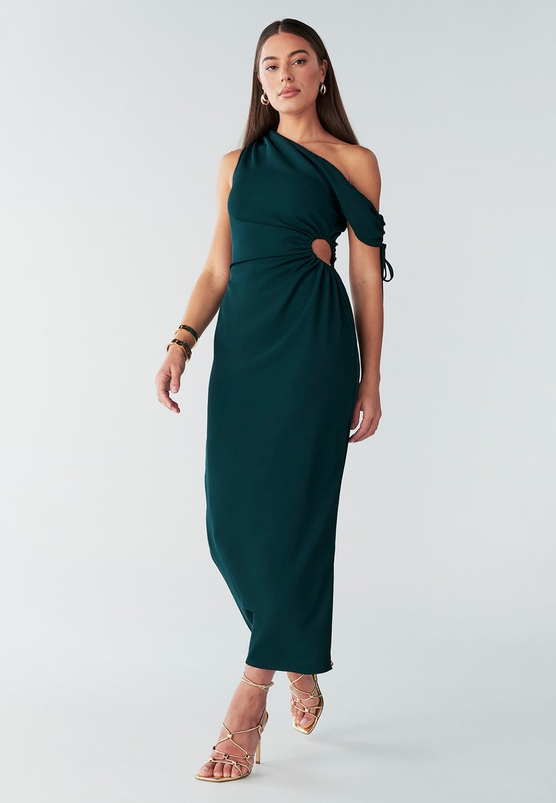 Vestito di colore verde acqua con una spalla scoperta, dettaglio arricciato sul lato e un'apertura circolare. Tessuto liscio, lunghezza alla caviglia, abbinato a tacchi dorati con cinturini.