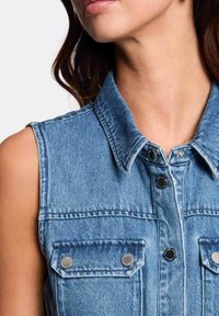 Denim mouwloze jas in lichtblauw. Voorzien van een spitse kraag, een sluiting met knopen aan de voorkant en twee borstzakken met zilverkleurige hardware accenten.
