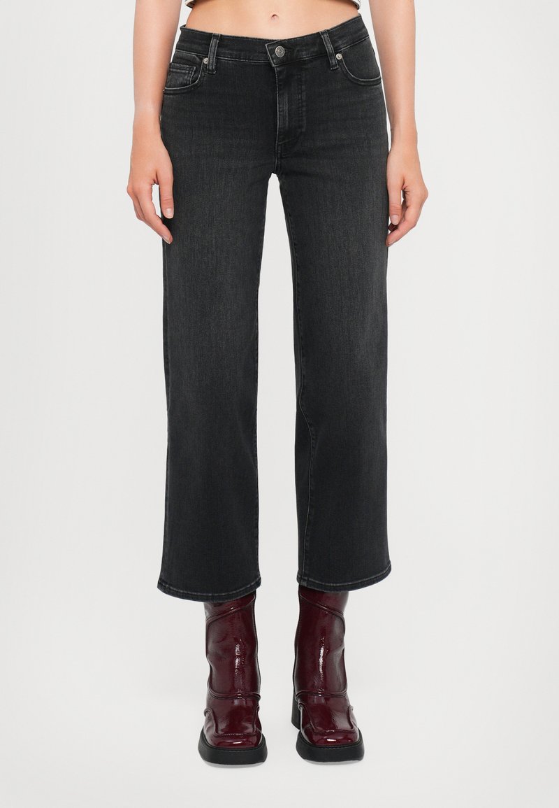 Black denim wide-leg jeans with a mid-rise waist, five pockets, and a slight fade. Paired with glossy burgundy ankle boots.