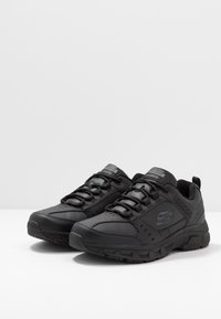 Black athletic shoes with synthetic upper, breathable mesh tongue, and sturdy rubber sole. Features laces and logo on the side.