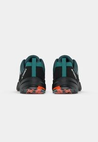 Um par de sapatos de hiking pretos e teal com solas laranja e cinza, mostrado por trás em um fundo branco.