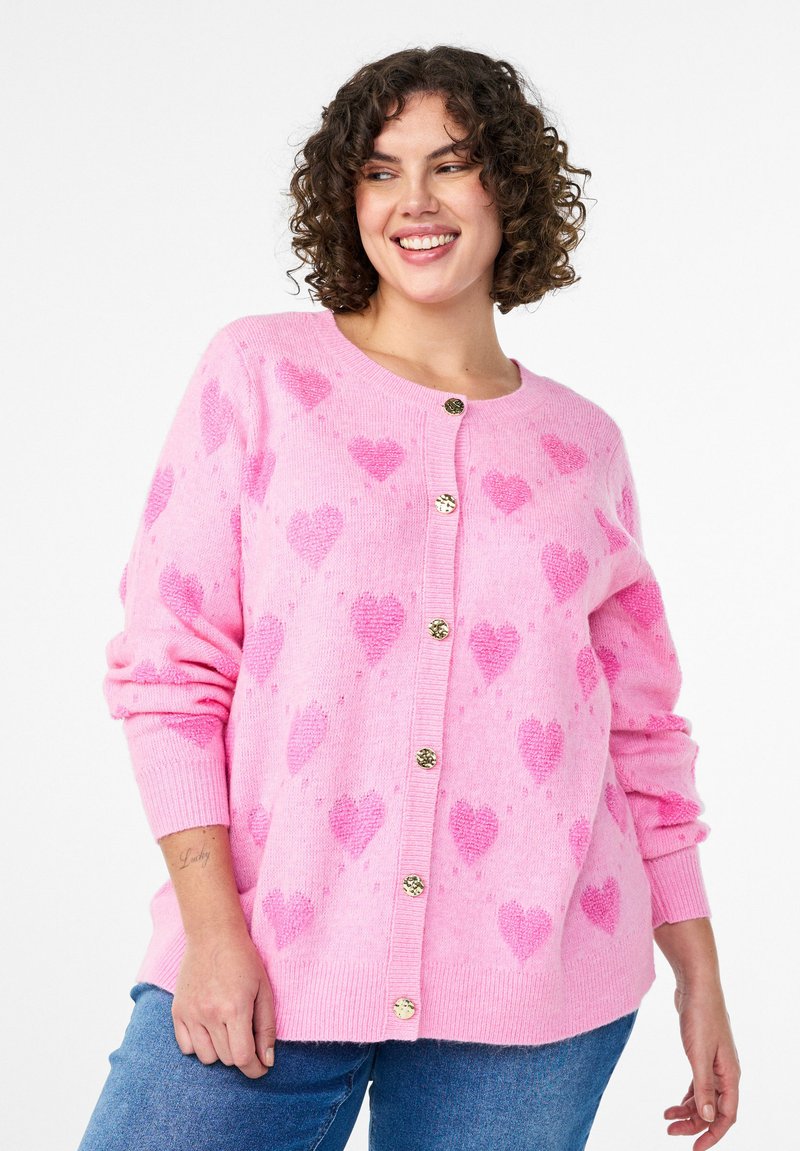 Roosa kardigan südamemustrite, ümarate kaelusaugu ja kuldsete nuppudega. Pehme tekstuur, pikkade varrukatega ja kergelt oversized lõikega.