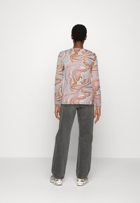 Långärmad tröja med ett marmorerat mönster i pastellfärger, kombinerad med högmidjade grå jeans och flerfärgade sneakers.