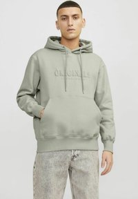 Sudadera verde con un bolsillo frontal, que presenta un texto en relieve "ORIGINALS". Tejido suave, cordones en la capucha y puños acanalados.