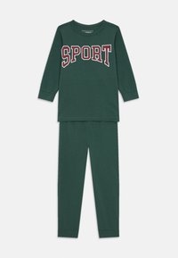 Groen lange mouwen top met "SPORT" in witte en rode letters, gecombineerd met bijpassende groene leggings. Zacht materiaal met een gladde textuur.
