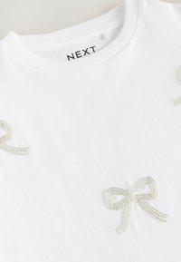 Hvid bomulds t-shirt med detaljerede perlekæde-designs. Rund halsudskæring, korte ærmer, glat tekstur og subtil glans.