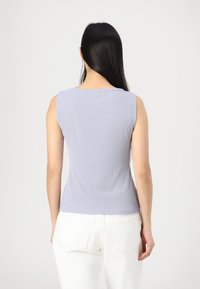 Lyselilla ribbet tanktopp med rund hals og ermeløst design, kombinert med hvite jeans. Glatt tekstur, tætsittende fasong.