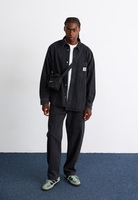 Chemise en denim noir avec fermeture à boutons, assortie à un pantalon noir. Sac bandoulière noir et baskets vertes avec des accents foncés.
