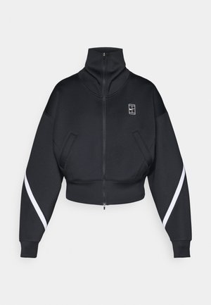 Jachetă neagră scurtă cu fermoar și guler înalt, având două buzunare frontale și dungi albe pe lateralele mânecilor. Material texturat.