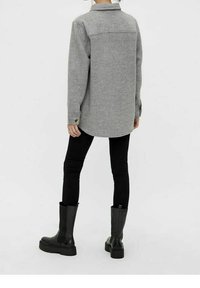 Graue, übergroße Hemdjacke aus Wollmischung mit spitzem Kragen und vorderen Knopfdetails, kombiniert mit schwarzen Skinny-Jeans und kniehohen Stiefeln.