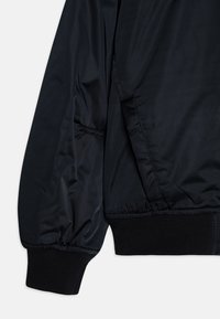Manga de chaqueta negra y dobladillo inferior con puños de canalé elásticos y un bolsillo diagonal en un tejido suave.
