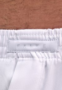 Tissu blanc avec un motif en chevrons, doté d'une étiquette de ceinture embossée du mot « FALKE ». La texture semble lisse et légèrement brillante.