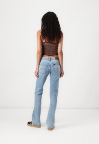 Crop top marrone con arricciature abbinato a jeans a zampa d'elefante di colore blu chiaro. Caratteristiche notevoli: tessuto strutturato, vita alta e logo Lee sul retro.