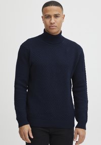 Pulover bleumarin cu guler înalt, realizat dintr-un material tricotat texturat. Prezintă mansete și tiv cu nervuri, având o croială modernă. Este potrivit pentru stratificare.
