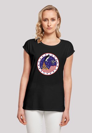 Black t-shirt with short rolled sleeves features a circular graphic of a rocket, an eagle, and stars on a blue background, with red and white accents.