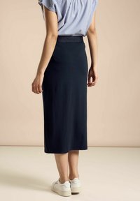Navy long skirt with a smooth texture and elastic waistband, paired with a striped light blue top and white sneakers.