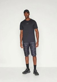 Melna sporta kreklā ar šauru piegriezumu, apvienota ar pelēkām biksēm ar polsterējumu un viļņotu rakstu. Izskatu papildina melnas zeķes un sporta apavi.