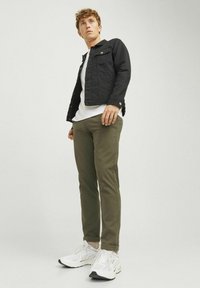 Jachetă din denim negru cu capse, tricou alb, pantaloni verzi măslinii și adidași albi. Design casual, ajustat, cu o textură netedă.