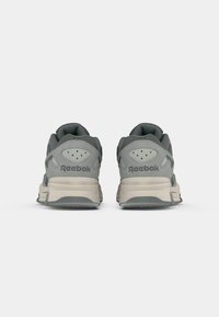 Par u sivih Reebok tenisica prikazanih s leđa, s bež srednjim potplatima, perforiranim panelima na peti i vidljivim logotipima brenda.