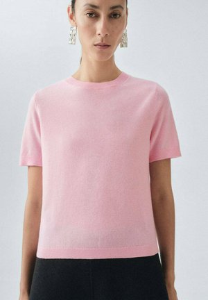 Maglione a maniche corte in misto lana color rosa pastello con scollatura rotonda e polsini a coste, abbinato a pantaloni neri.