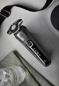 Rasoio elettrico Philips, nero con accenti metallici, tre teste rotonde, display LCD e pulsante di accensione. Superficie testurizzata grigia sullo sfondo.