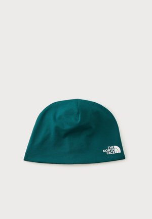 Berretto in tessuto morbido verde scuro con il logo The North Face bianco sul bordo inferiore su uno sfondo chiaro uniforme.