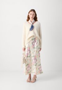 Suéter de punto oversized en crema con escote en pico, combinado con una falda maxi de estampado floral en tonos pastel. Accesorios ligeros y sandalias beiges completan el look.