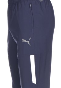 Marineblauwe sportbroek gemaakt van vochtregulerend materiaal, met een ritszak, witte accentstreep en reflecterend logo.