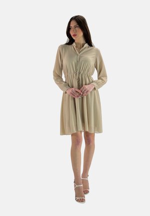 Beige Hemdblusen-Kleid mit langen Ärmeln, tailliertem Bund und fließendem Rock. Leichter Stoff mit glatter Textur, kombiniert mit weißen Riemchen-Heels.