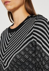 Schwarzer und silberner gestreifter Pullover mit geometrischem Muster, Rundhalsausschnitt und dekorativen Knöpfen an der Schulter. Rippstruktur.