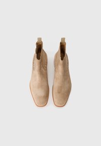 Botines de ante beige con un acabado suave, punta afilada y costuras decorativas a lo largo de los lados. Presentan asas de tirón para un fácil uso.
