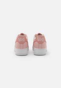 Rosa lädersneakers med vit gummisula, med vit broderad "NIKE"-logotyp på baksidan. Designen inkluderar en slät yta och rundad form.