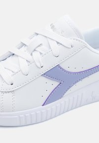 Hvite joggesko med lilla sideaccent, laget av syntetisk lær med perforeringer, flate snører og teksturert gummisåle.