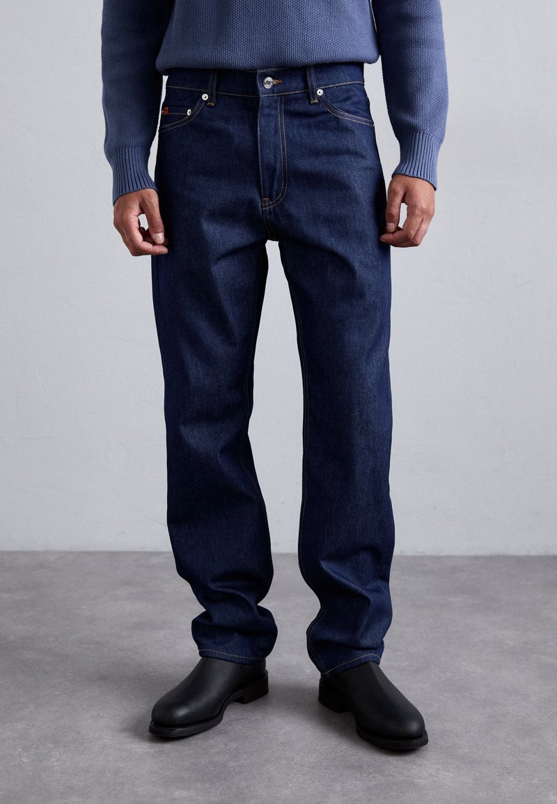 Jeans de mezclilla azul marino con un diseño clásico de pierna recta, que presentan costuras en contraste de color naranja y un cierre de botón en la cintura.