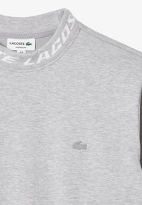Felpa grigia con finitura testurizzata, dotata di un collo rotondo a coste con il marchio "LACOSTE" ripetuto e un piccolo logo coccodrillo ricamato.