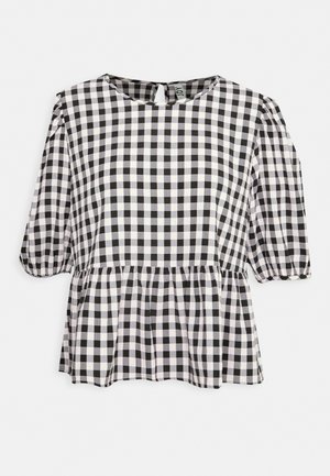 Blouse à carreaux noirs et blancs avec manches courtes bouffantes et détail peplum froncé à la taille sur un fond uni.