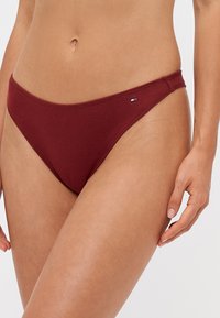 Tanga burgundy cu dungi, cu un design cu talie joasă și un mic logo al mărcii pe lateral, având o textură netedă.
