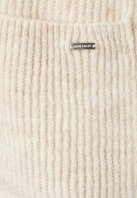 Strickpullover in hellcreme Farbe mit einem gerippten Muster. Mit einem kleinen silbernen Etikett, das "MORE & MORE" eingraviert hat. Weiches, warmes Material.