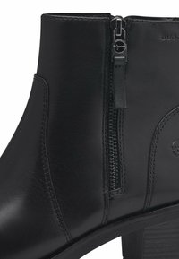 Botín negro de cuero hasta el tobillo con cremallera lateral, textura suave, puntera redonda y tacón cuadrado. Presenta un diseño minimalista y costuras sutiles.